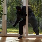 A burglar in dark clothing entering a house through a glass door