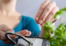 Person seasoning food with herbs from a pot