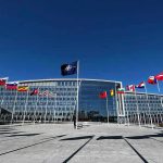 Russian Drones Invade Poland—NATO Scrambles! Flags outside NATO headquarters building under clear blue sky.