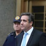 Man in suit walking outside with security officers.