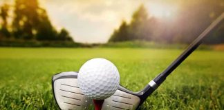 A golf ball on a tee with a golf club resting beside it on green grass