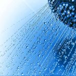 Close up of a shower head with water droplets against a blue background