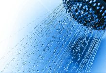 Close up of a shower head with water droplets against a blue background