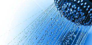 Close up of a shower head with water droplets against a blue background