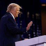 Person speaking at a podium with hand raised