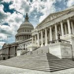 Capitol building with columns and cloudy sky.