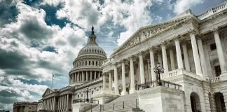 Capitol building with columns and cloudy sky.