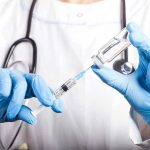 Doctor filling syringe with vaccine from vial.