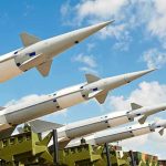 Multiple missiles pointed upward on launchers against blue sky.