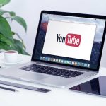 Laptop displaying YouTube, with coffee and stationery nearby.