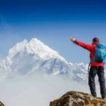 Hiker with arms outstretched in front of snowy mountains.