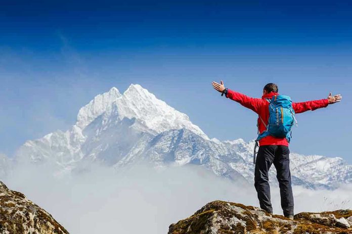 Hiker with arms outstretched in front of snowy mountains.