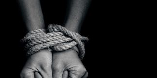 Two hands tightly bound with rope against a dark background