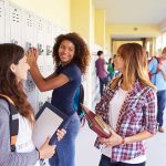 Three high school students interacting near lockers in a hallway