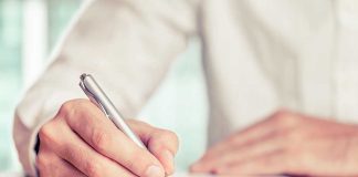 A hand holding a pen writing on a document in an office setting