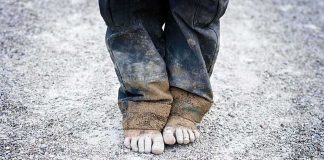 A child standing barefoot on a gravel surface with dirty pants