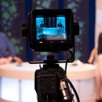 Camera focused on a television studio interview with two seated hosts