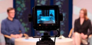 Camera focused on a television studio interview with two seated hosts