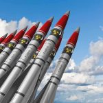 A row of military missiles with red tips and nuclear symbols against a blue sky
