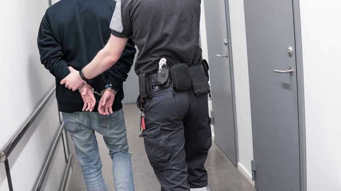 1082126789 Officer escorting handcuffed person down hallway.