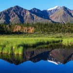 Scenic view of mountains reflecting in a calm lake surrounded by greenery