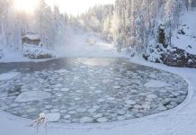 TERRIFYING: Ice Breaks, Girls Disappear Below A serene winter landscape featuring a frozen lake surrounded by snow-covered trees and a log cabin