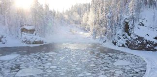 A serene winter landscape featuring a frozen lake surrounded by snow-covered trees and a log cabin