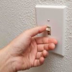 A hand reaching to turn on a light switch on a textured wall