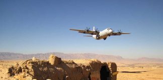 Military aircraft flying over a desert with an abandoned bunker and a for sale sign