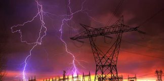 Lightning strikes illuminate a power station against a colorful sunset sky