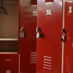 Locker Room SPY Cam Horror Rocks School Red lockers with padlocks, one open with hanger.