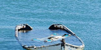 Half-submerged, weathered, abandoned boat floating on calm water.