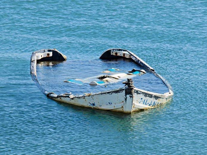 20081782 Half-submerged, weathered, abandoned boat floating on calm water.