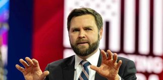 Man in suit gesturing with hands on stage.