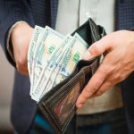 Person holding wallet full of hundred dollar bills