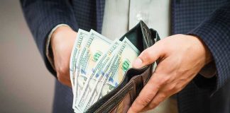 Person holding wallet full of hundred dollar bills