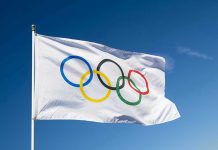 Olympic flag waving against clear blue sky.
