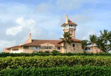 Large pink mansion with tower, palm trees, and garden.