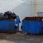 Trash Bag Horror SOLVED After 47 Years Two blue dumpsters, one overflowing with trash bags.