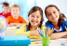 UK Schools TRANSITION 4-Year-Olds Two smiling girls in a classroom with colorful stationery and classmates in the background