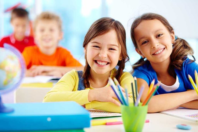 shutterstock_130517294.jpg Two smiling girls in a classroom with colorful stationery and classmates in the background