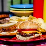 A plate with a hamburger, hot dog, and potato chips on a picnic table