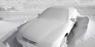 A car completely covered in snow, surrounded by a winter landscape