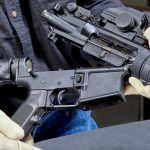 Gunfire Erupts On U.S. Air Base Person assembling a black rifle with gloves on.