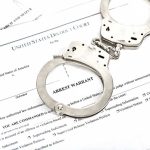 Handcuffs on top of an arrest warrant document.