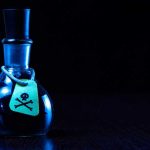 Grief Author On Trial For Poisoning Husband Dark bottle with skull-and-crossbones label on table.