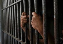 Hands gripping prison cell bars tightly.