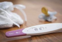 A pregnancy test next to a pacifier and a knitted baby hat on a wooden surface