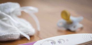 A pregnancy test next to a pacifier and a knitted baby hat on a wooden surface