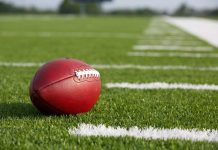 A red American football resting on a green artificial turf field